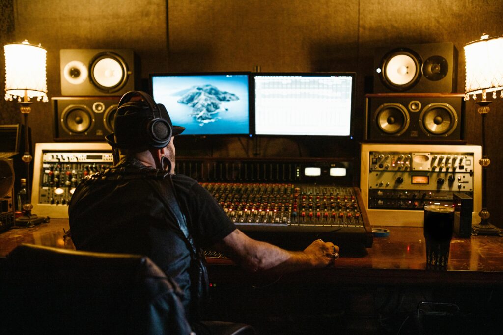 Music producer sitting at audio mixer in professional recording studio.